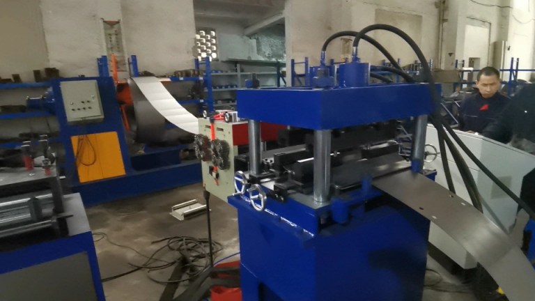 Imagen de una instalación industrial que muestra un desenrollador hidráulico con una gran bobina de acero, conectado a un mecanismo alimentador servo amarillo, preparando el acero para su posterior procesamiento.