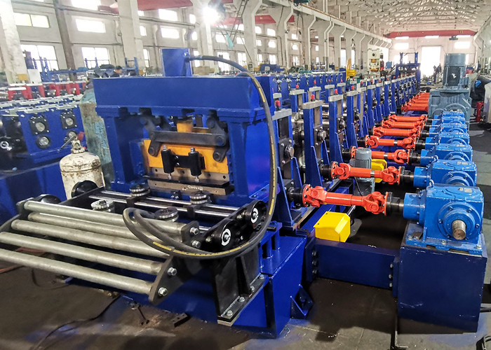 Una larga máquina industrial azul de perfilado de rodillos con numerosos juegos de rodillos, que alimenta una lámina plana de metal a su secuencia de matrices de conformado.